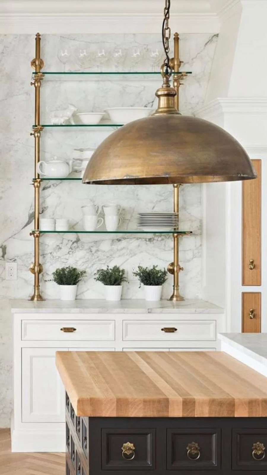 white kitchen design with antique brass pendant light and open shelving for ceramic dishware. a black island with butcher top countertop sits in the middle of the space