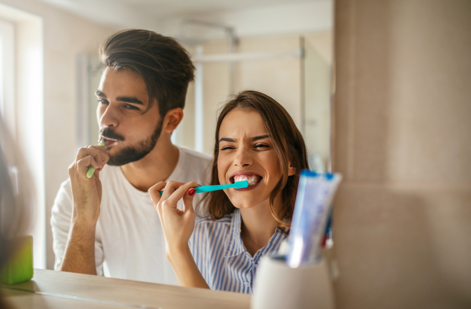 young couple brushing their teeth while looking in a mirror