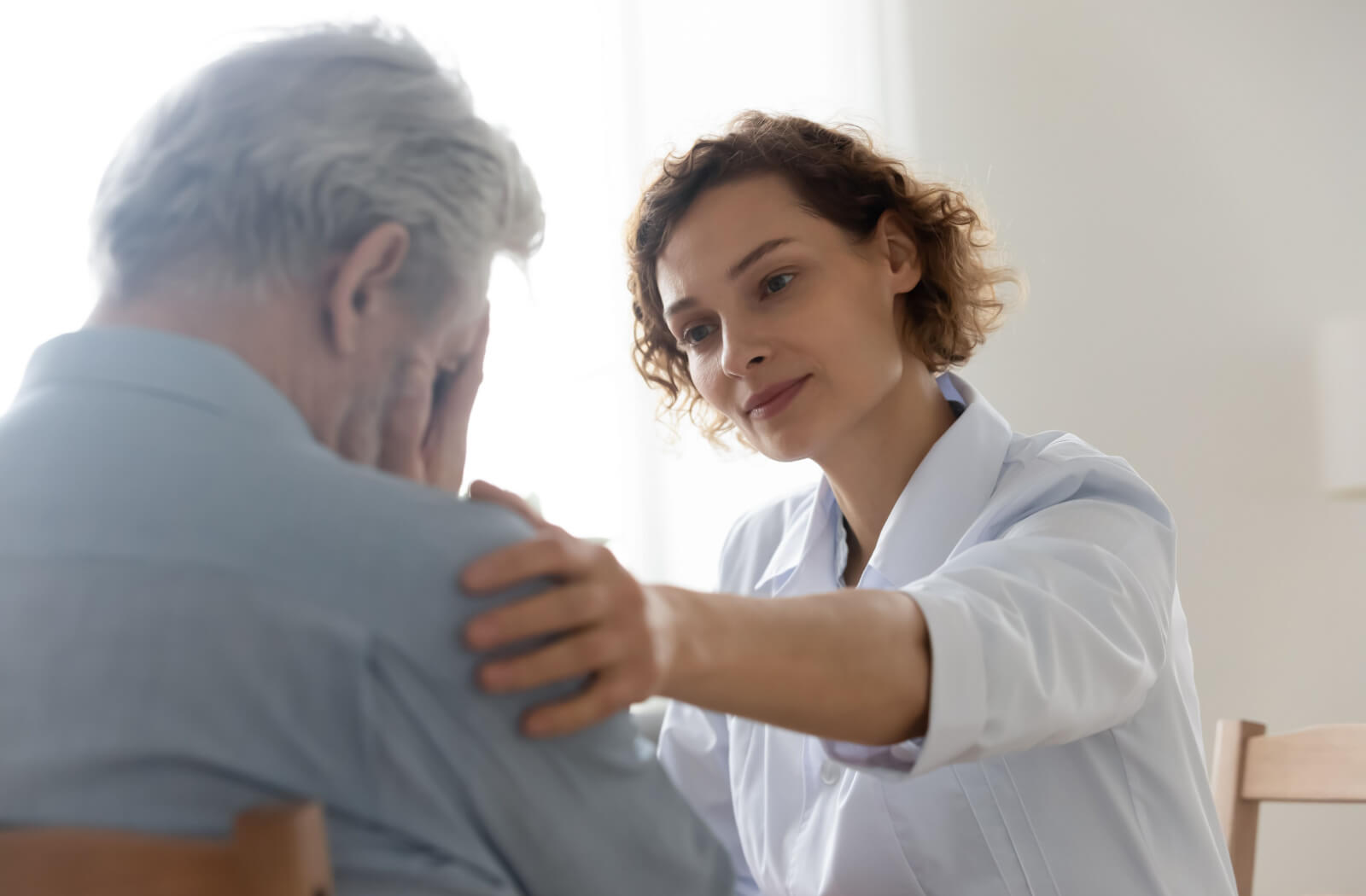 A young female nurse is comforting an upset mature male patient due to mood changes because of dementia.