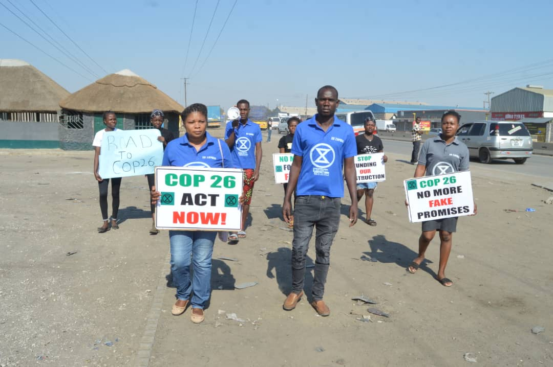 8 rebels walk down a wide dirt road with signs about COP26.