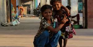 File: Two children pose for a photograph as their mum washes their clothes on a street in Old Delhi on October 14, 2010 in Delhi, India.