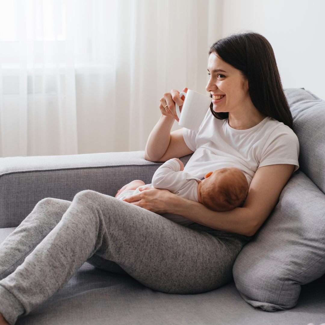 Mother drinking from a mug while breastfeeding her baby