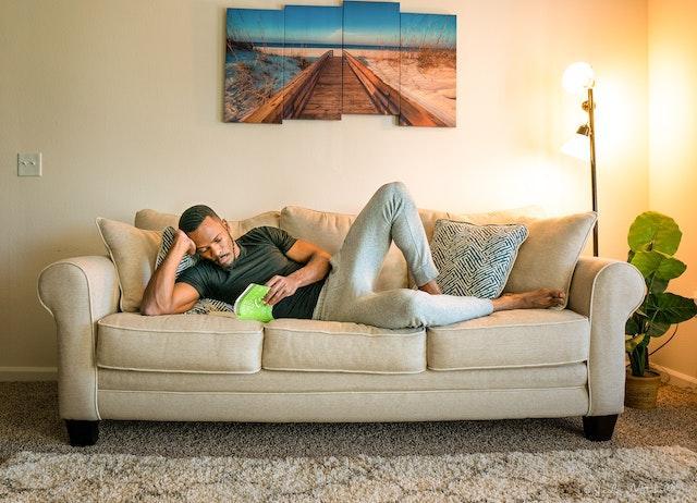 A man reading a book on his couch as he bought a home on a single income.