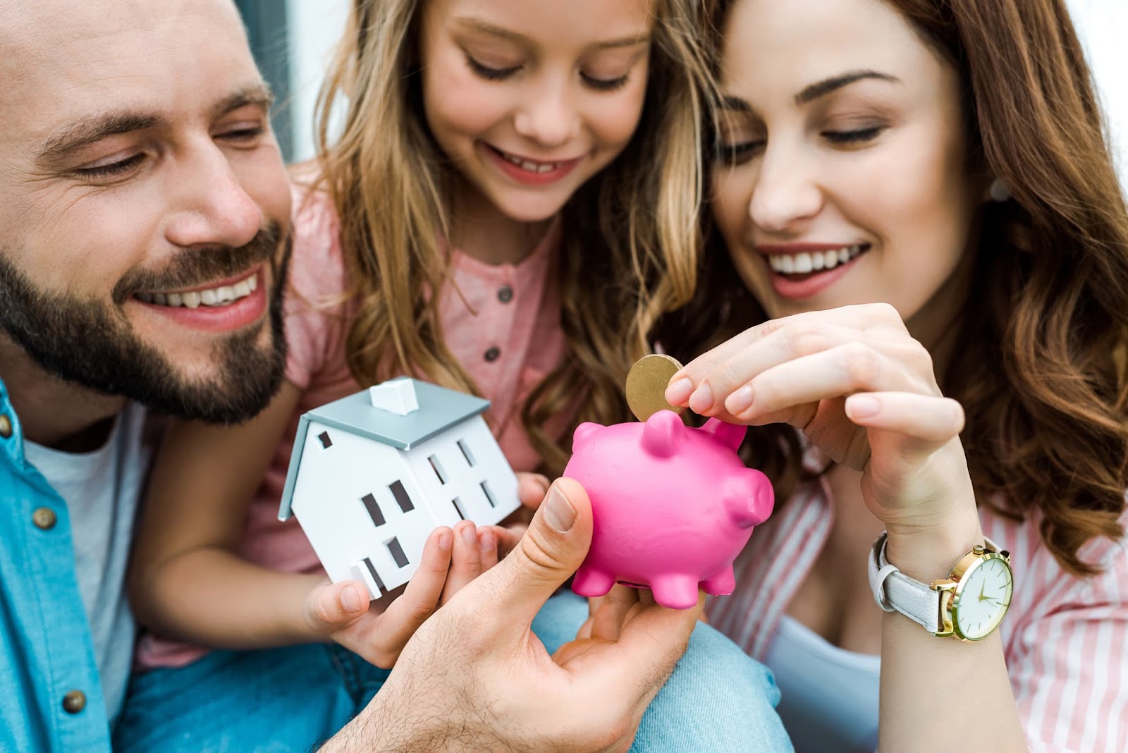 Familia poniendo una moneda en una hucha para poder comprarse una casita