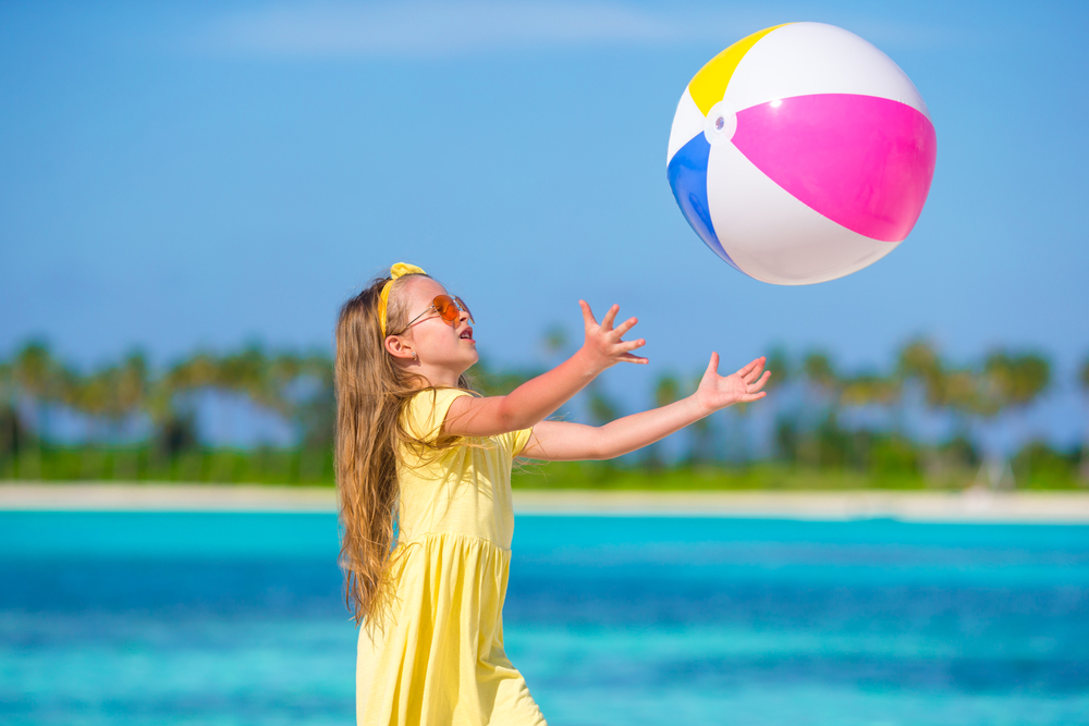Little girl playing on beach with ball