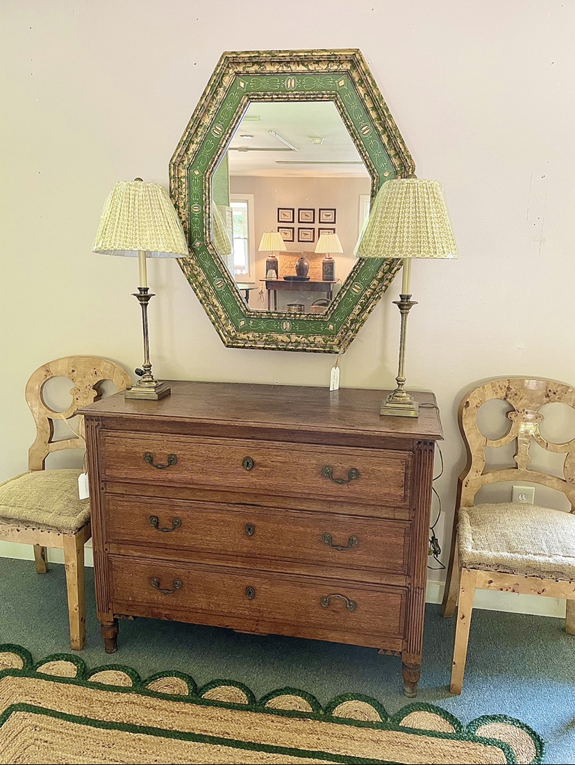 A wall mirror above a staged antique chest of drawers, reflects the room.