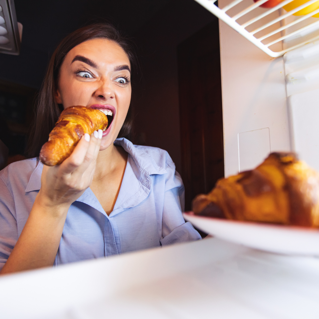 Hungry woman eating a croissant and staring at another in the refrigerator before breastfeeding
