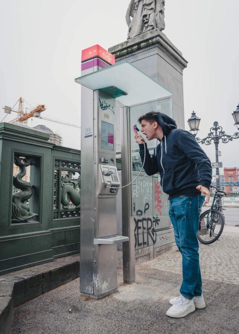 man in black jacket and blue denim jeans standing near black telephone booth during daytime