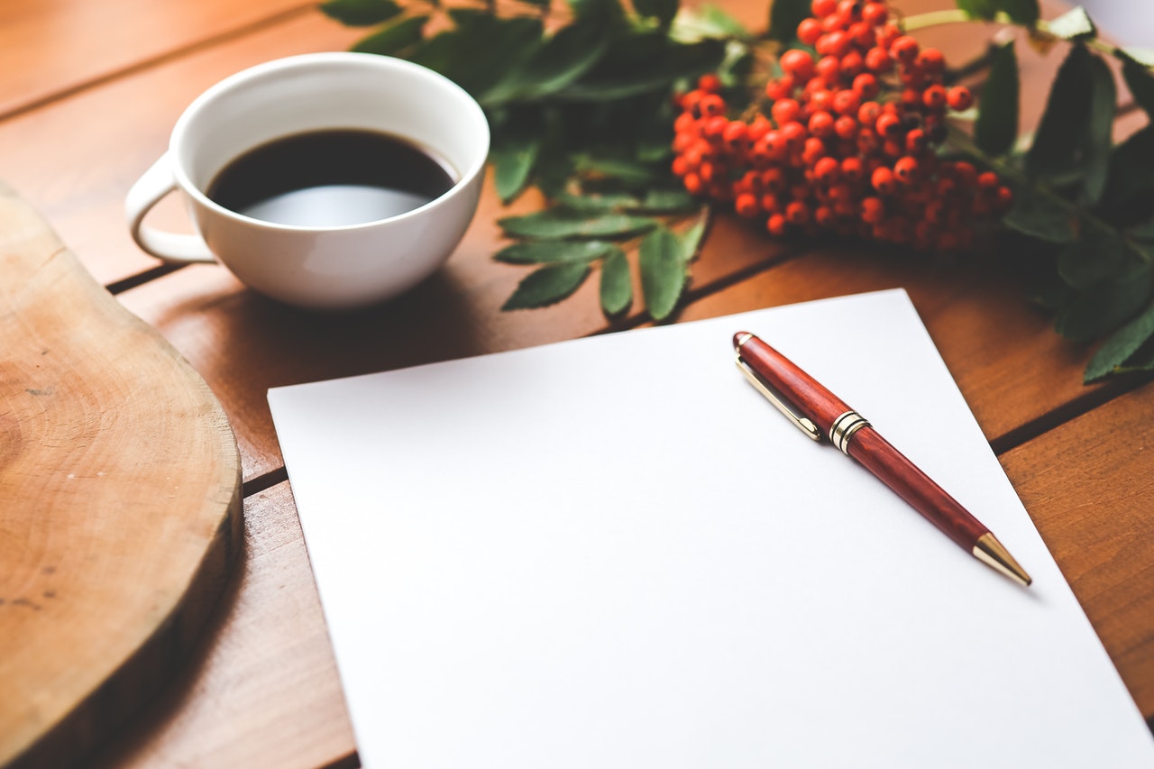 Een notitieblok, een koffiemok en een pen op een bureau binnenshuis