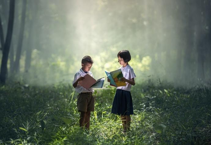 Two children reading books in the forest.