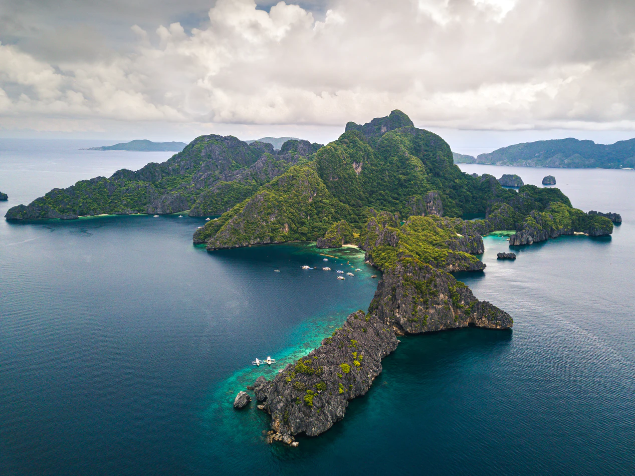 Large island with rock formations and boats surrounding it.