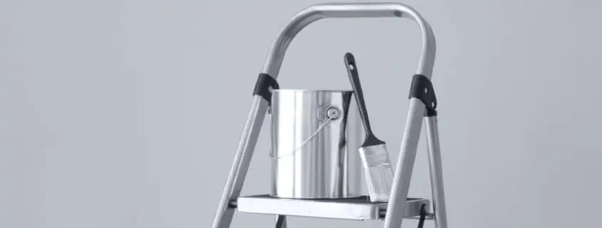 A silver stool with a paint bucket and paint brush on the top step.