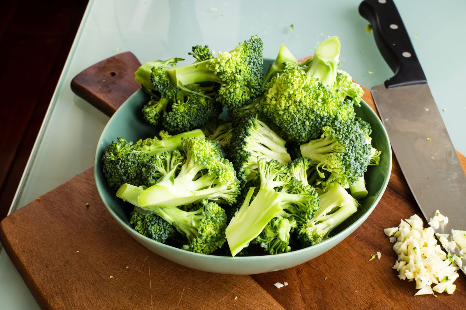 broccoli in a bowl beside knife and wooden chopping board