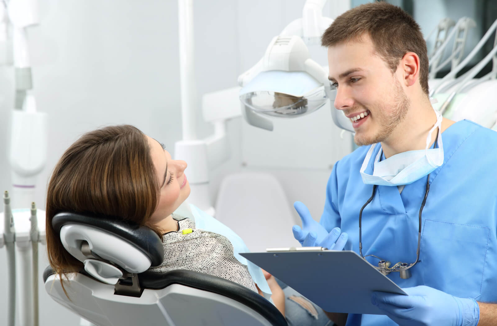 A male dentist in blue scrubs  explaining a dental treatment procedure to  a woman sitting in a dentist's chair