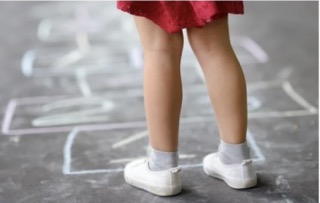 Girl's legs wearing white shoes and socks standing in front a hop scotch grid