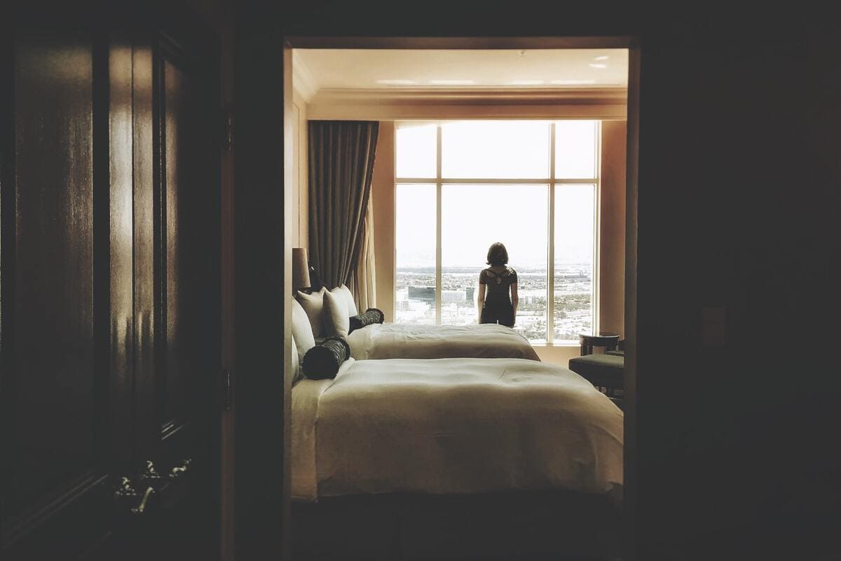 Un ragazza che guarda fuori dalla finestra all'interno di una stanza di hotel