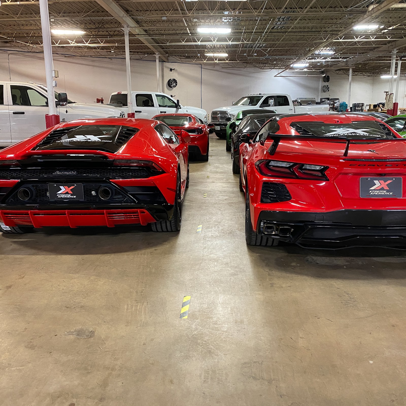 A red Corvette C8 and red Lamborghini Huracan EVO, both 2020 model years sit in the Xtreme Xperience garage bright and shiny.