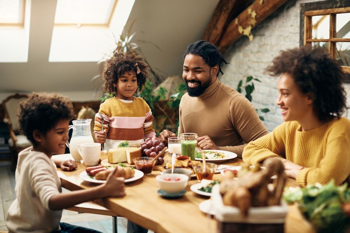 Família reunida ao redor de mesa para tomar seu café da manhã. Pessoas alegres, um homem e uma mulher e um casal de crianças