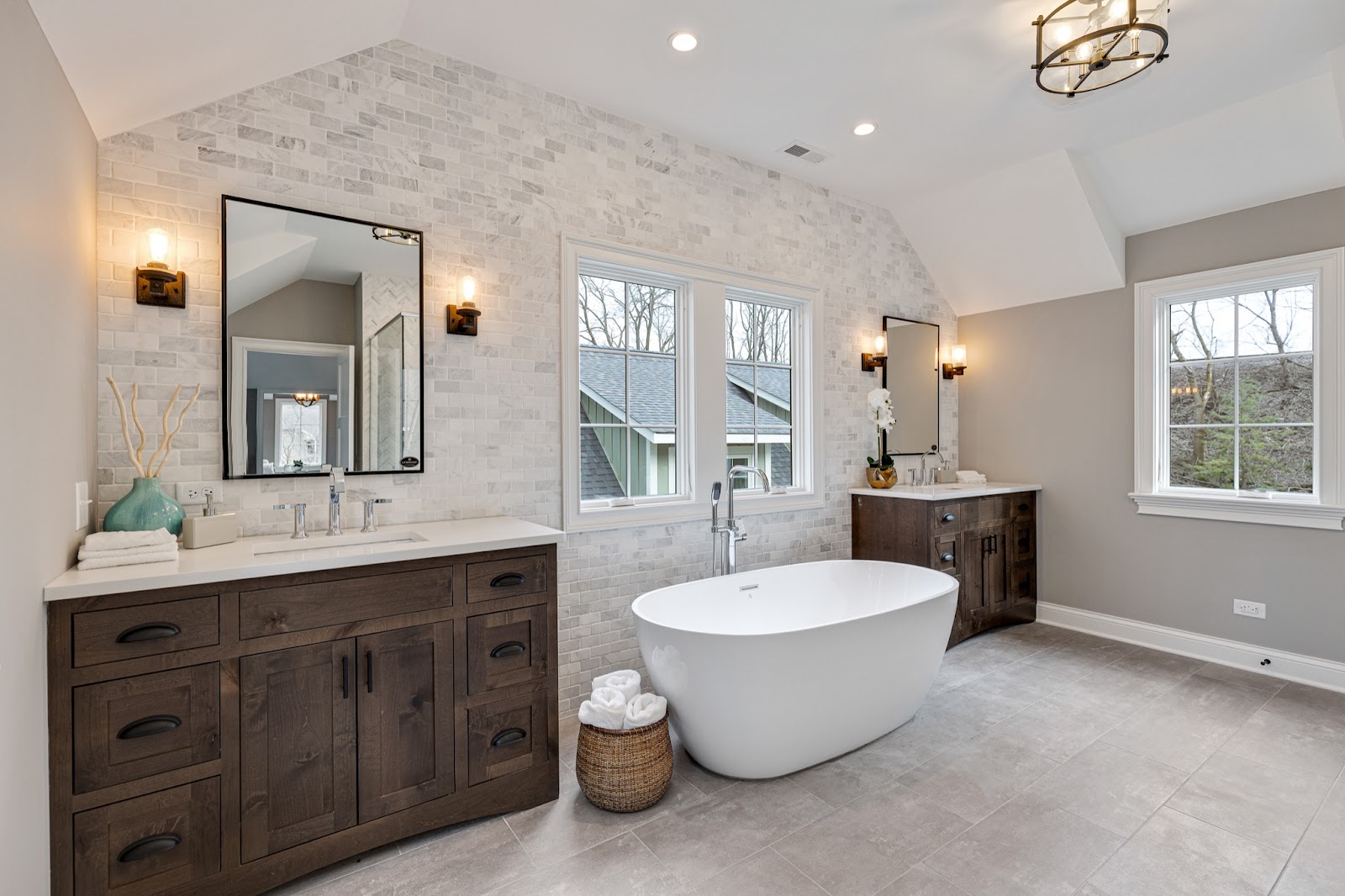Modern spa master bath with marble tile, natural wood vanities and a large soaking tub underneath a  picture window.