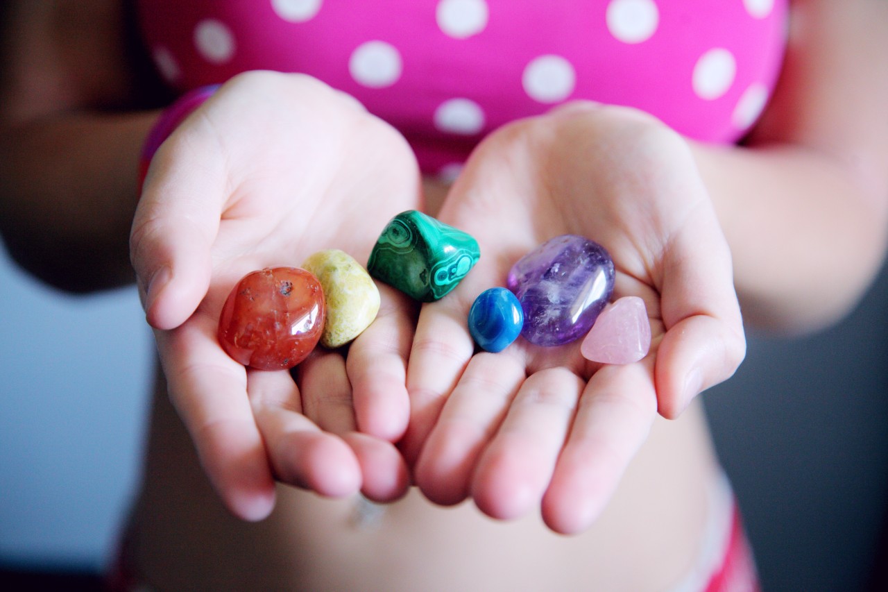 A child has both of her palms out holding various polished stones in her hand.