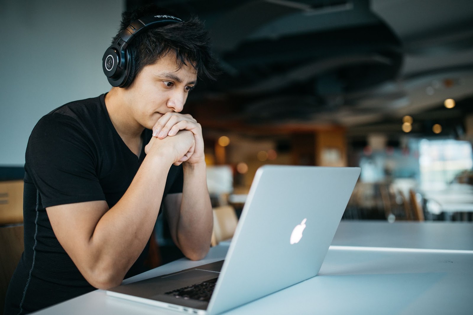 A picture of a young man, wearing headphones, staring pensively at his Mac laptop.