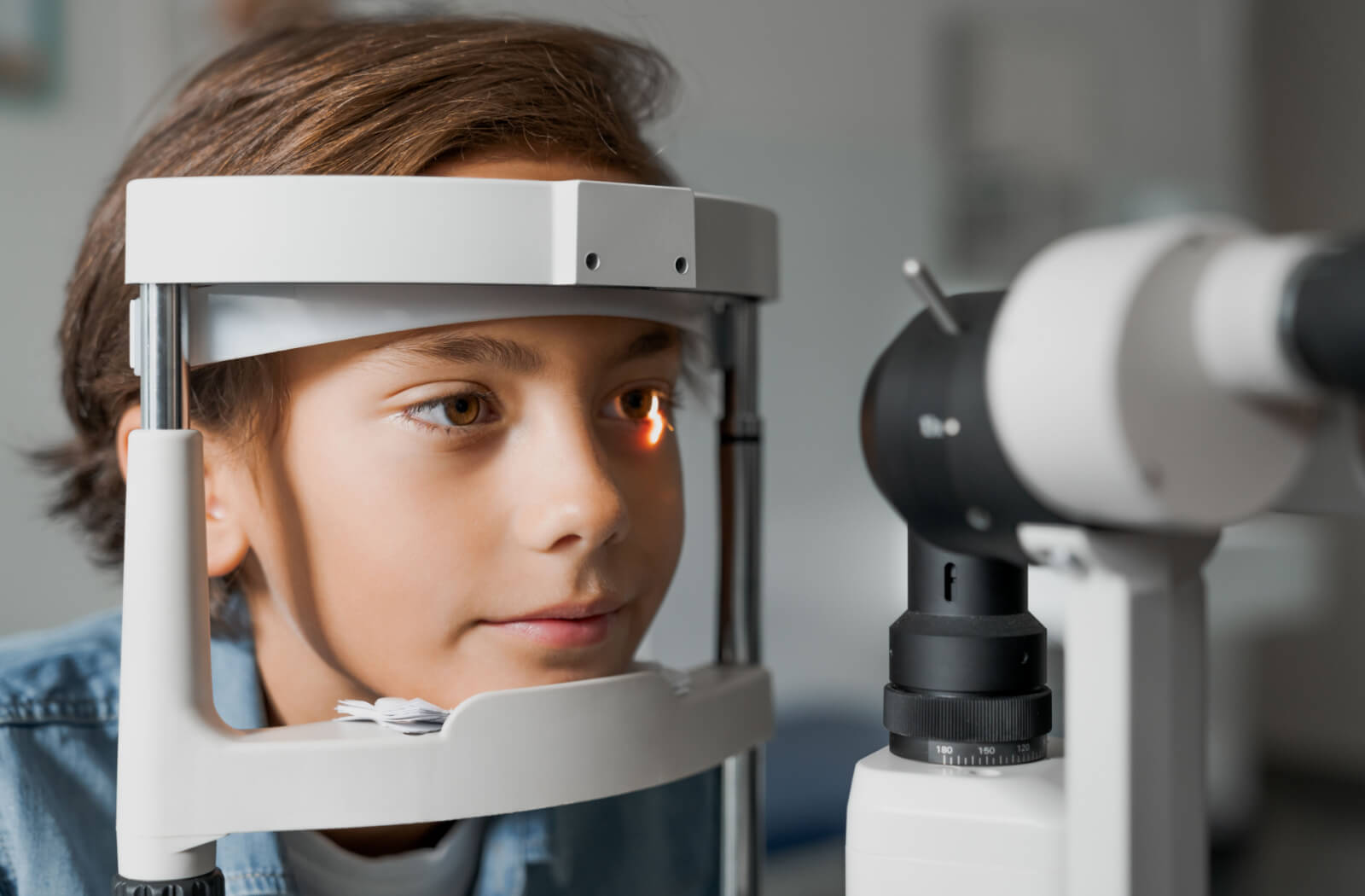 A male child sitting in an optometrist's office looking into a machine that tests his vision.