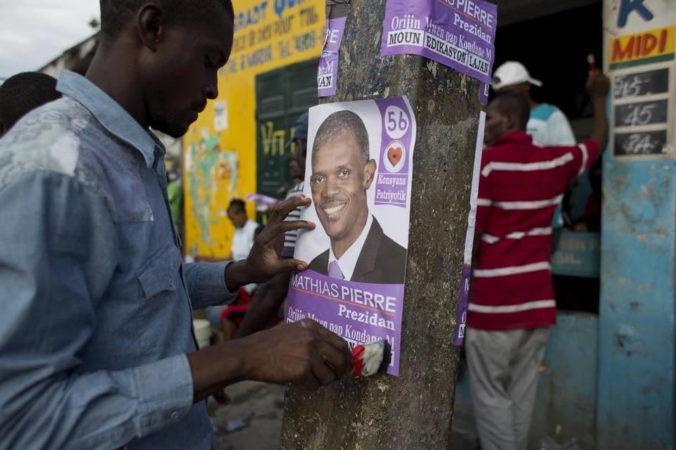 In this Oct. 3, 2015 photo, a man pastes to a pole a campaign poster of presidential candidate Mathias Pierre, in Port-au-Prince, Haiti. Cities and towns across Haiti are plastered with colorful campaign ads, leaving voters struggling to differentiate a swarm of candidates who grin from posters, banners and billboards slapped on nearly everything that doesn't move and a few that do. In the first round of Haiti's presidential vote on Oct. 25, voters will choose from a field of 54 candidates.