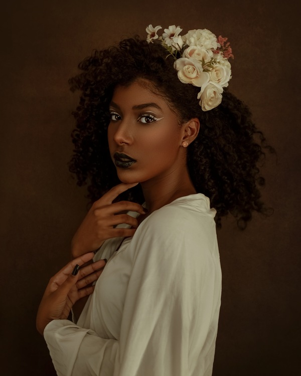 foto de uma mulher negra com a mão no queixo e uma flor no cabelo