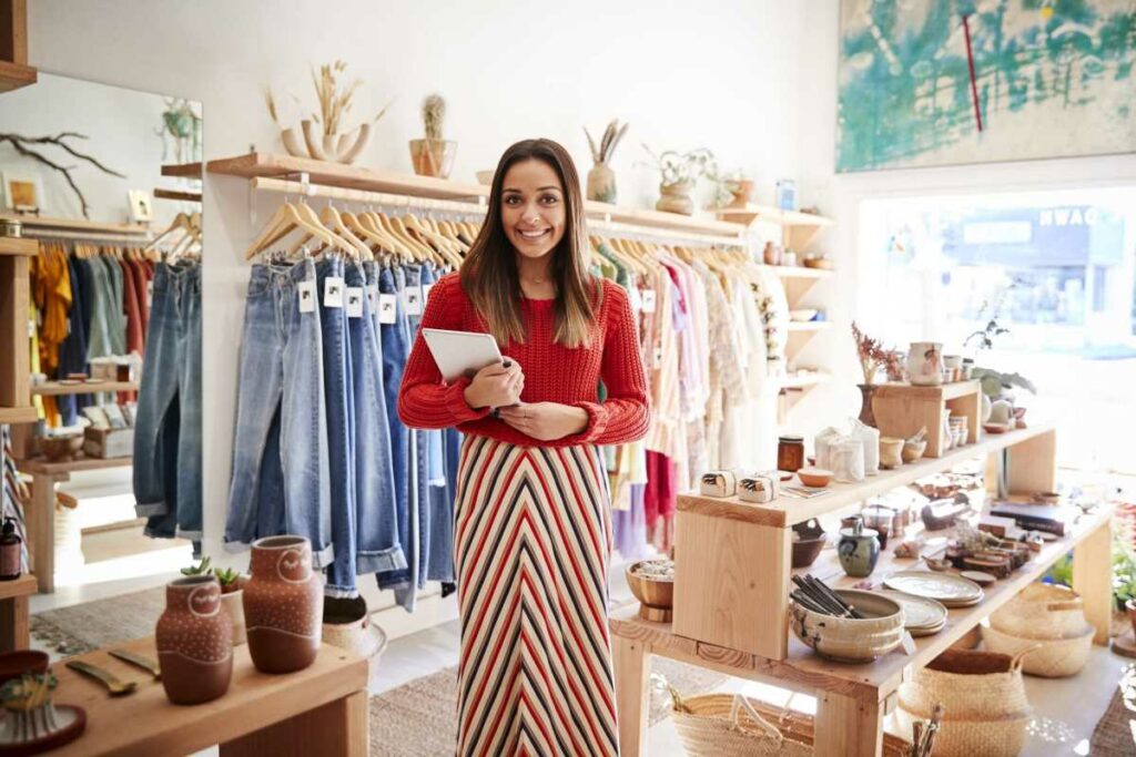 Smiling owner of small business stands in shop holding tablet