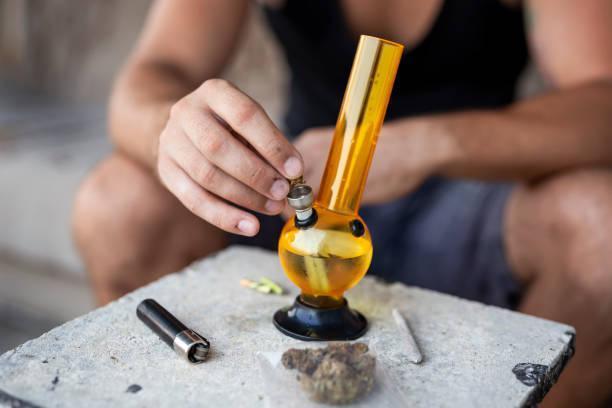 Man filling up bong with cannabis Young man smoking pot using bong; detail of male hand filling up bong with cannabis, getting it ready for use water pipe smoking stock pictures, royalty-free photos & images