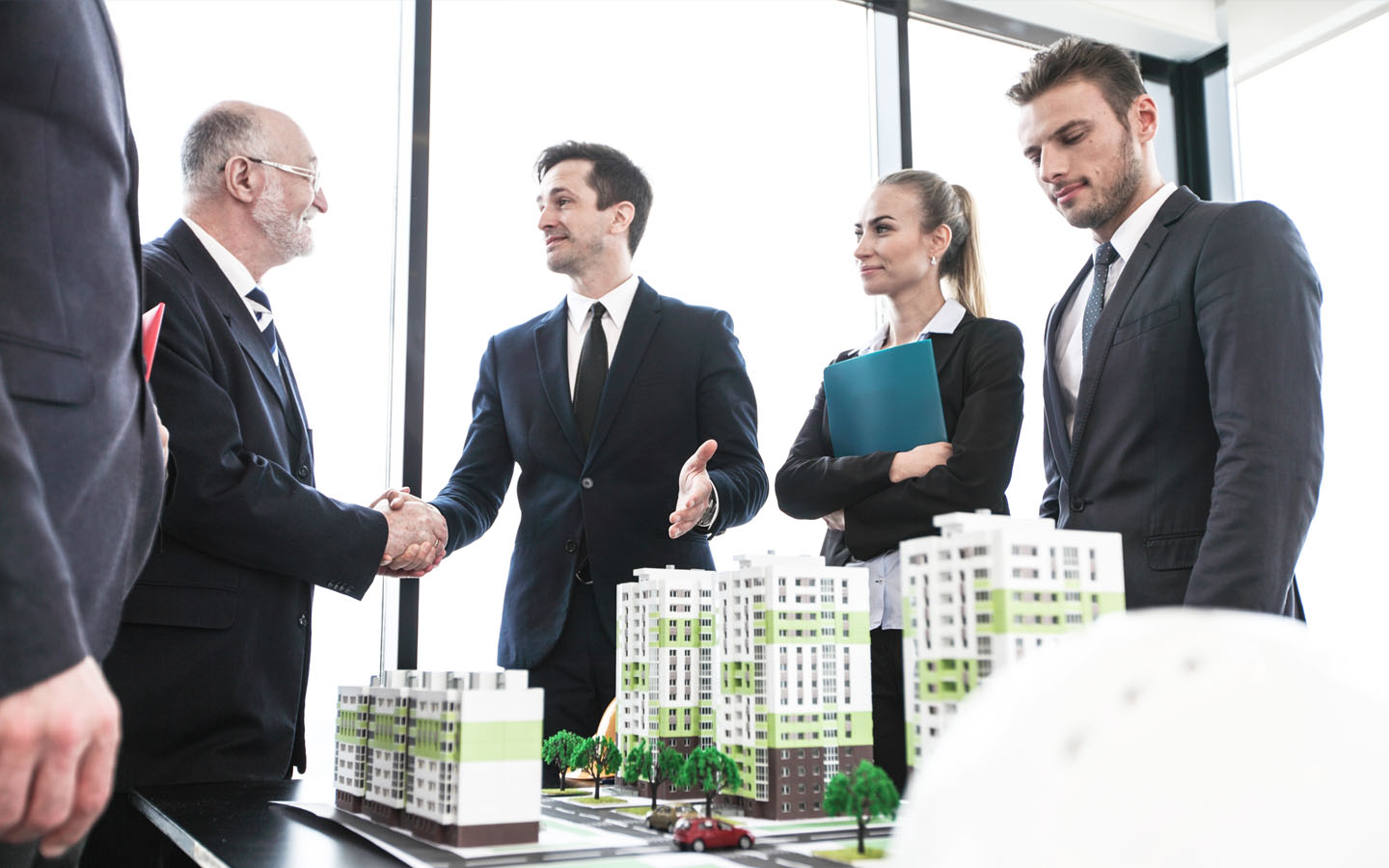 business people finalising deal with a property model placed on table. want to learn how to start a real estate business? start by studying the market
