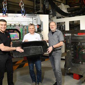 Pleased with a successfully manufactured load compartment recess made of glass-fibre reinforced polypropylene for the EQS from Mercedes-Benz. From left: Anton Liebl, Siebenwurst project manager, Bernd Hilneder, Oerlikon Hrsflow, and Michael Bilo, Oerlikon Balzers. To the right and behind them, respectively, one of the iridescently coated mould halves for the production of the component can be seen.