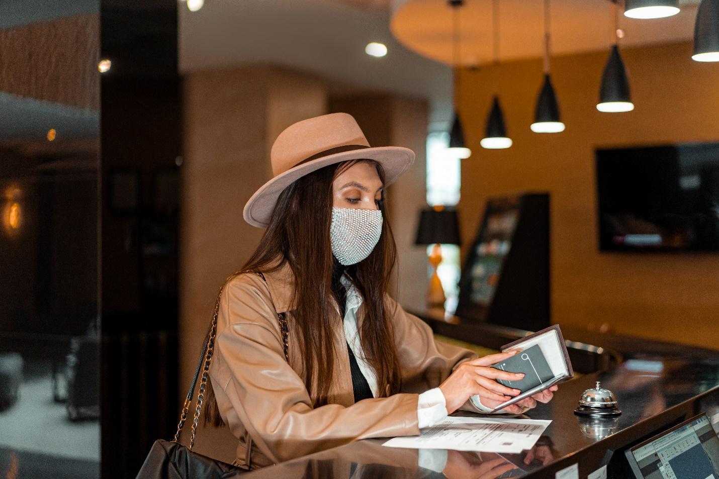 A person wearing a face mask and a hat sitting at a counter

Description automatically generated