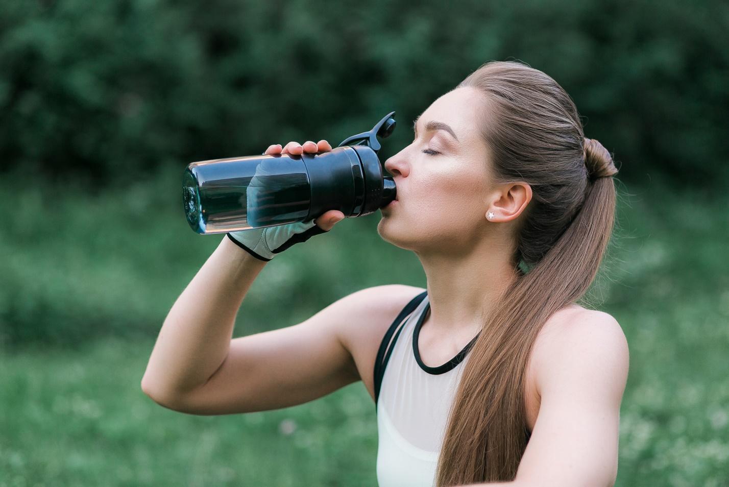 beautiful-girl-sport-clothes-drinking-water-after-workout-while-sitting-grass