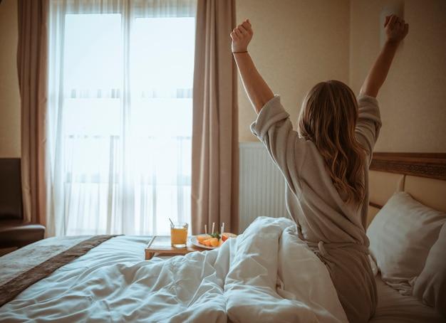 Vista traseira de uma mulher se espreguiçando com itens de cestas de café da manhã sobre a cama