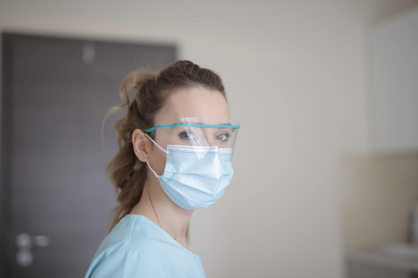 a person wearing scrubs, a face shield, and a mask
