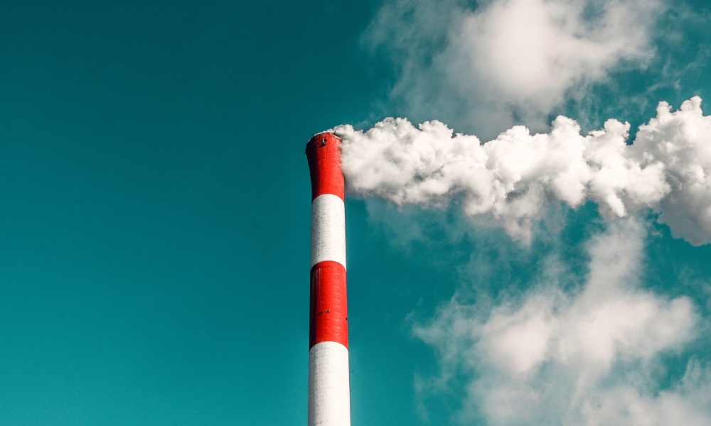 Image of industrial vent producing smoke against a blue sky. 