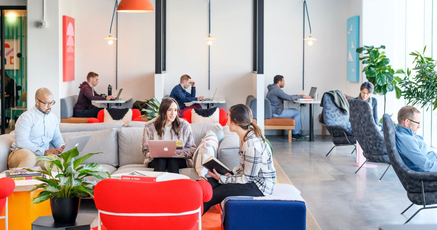 interior of a wework with some people working at individual booths and others using a collaborative area to work