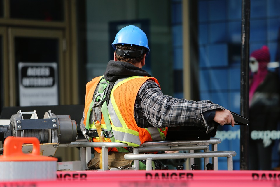A construction worker in an orange vest next to red danger tape.