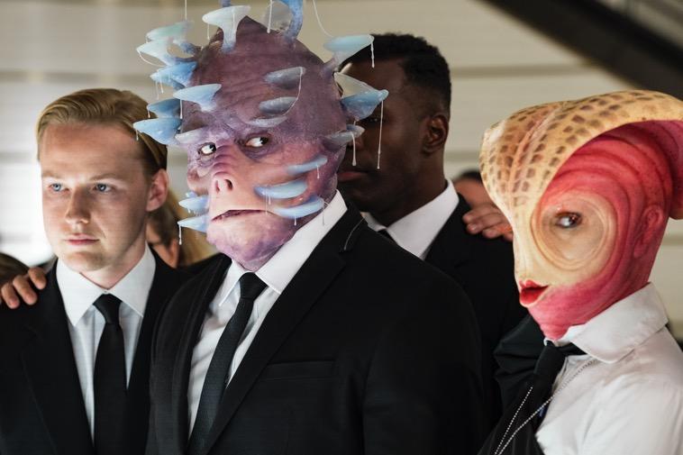 A group of people standing next to a person in a suit and tie

Description automatically generated