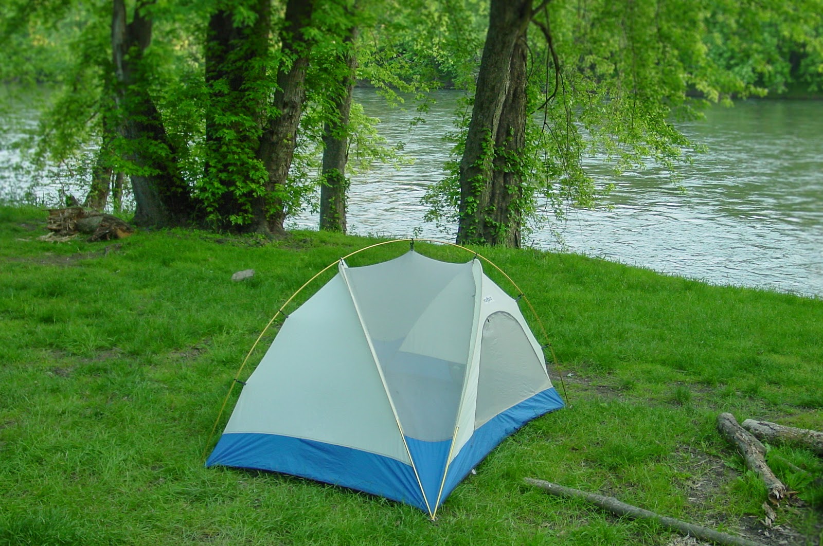 A tent on green grass with water and trees. 