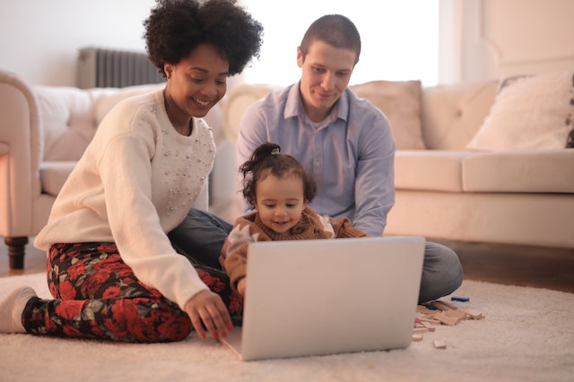 parents guiding infant through play on laptop computer