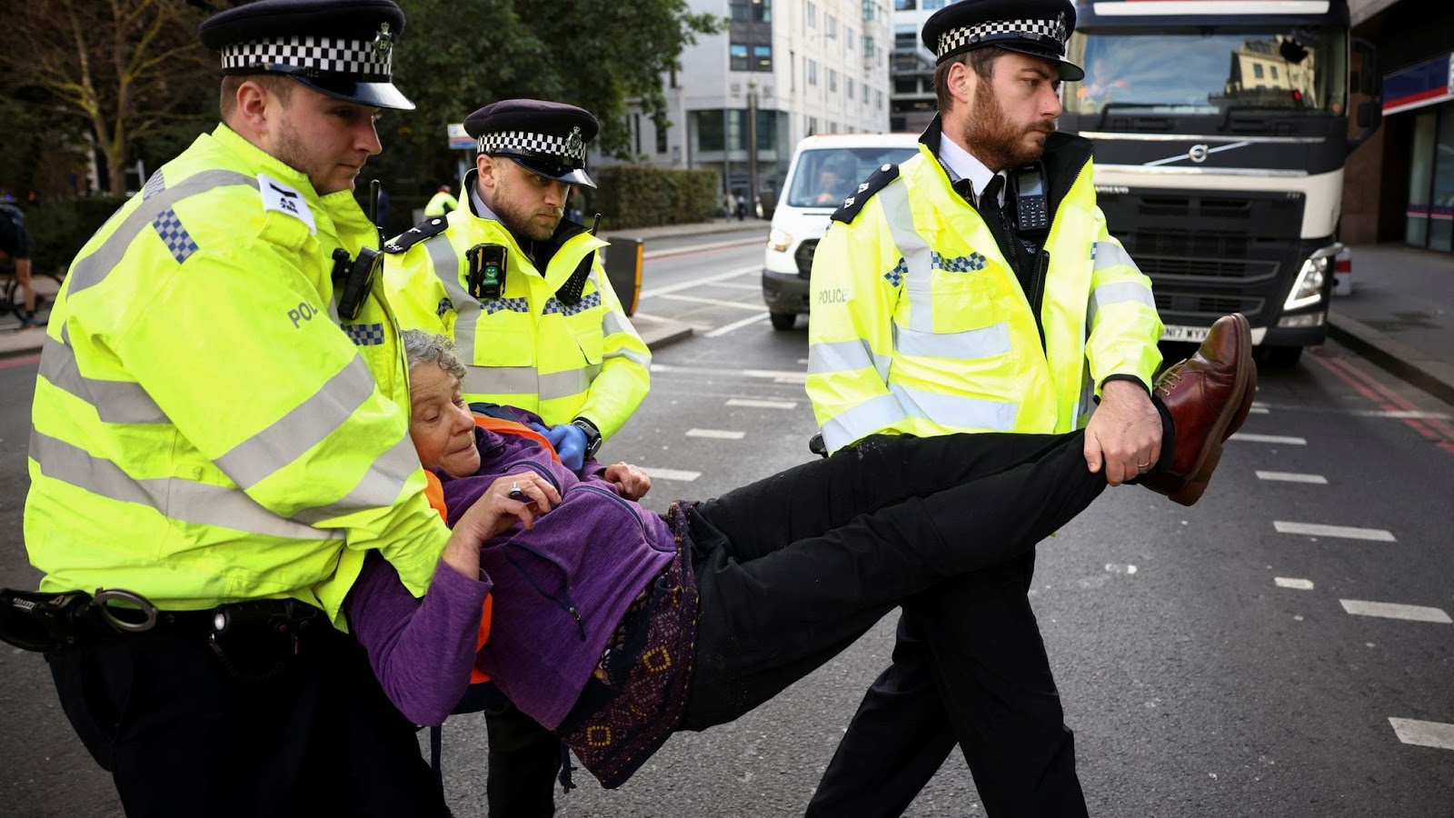 Marguerite is carried across a London road by three police officers.