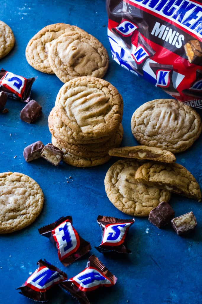 stacked cookies with bag of snickers in background and unwrapped mini snickers around. 