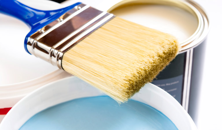 A paintbrush resting on top of three open paint cans