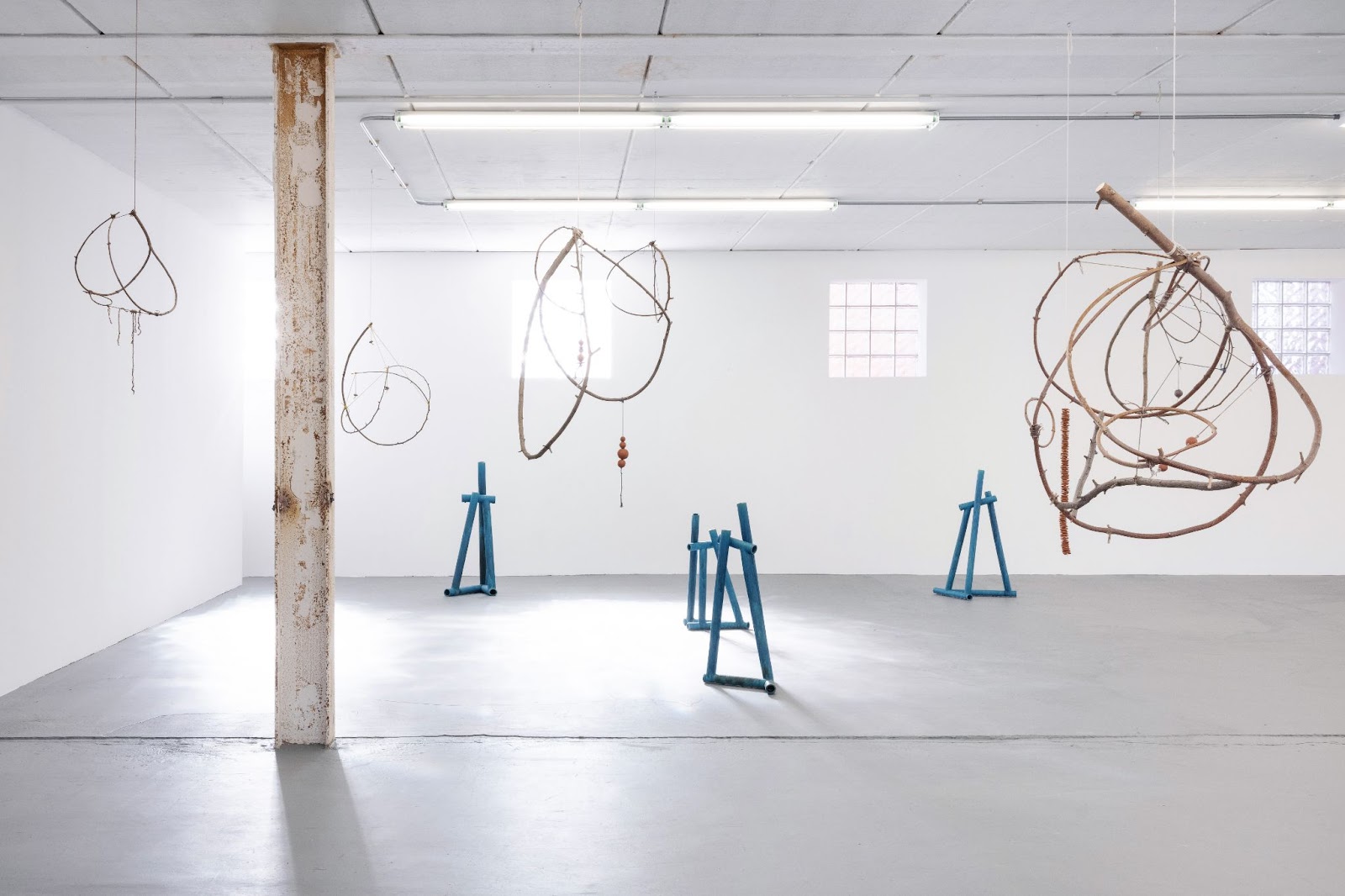 Image: Tetsuya Yamada, Shallow River, 2022. Installation view. In a bright white room, four mobiles made of curving sticks and wire hang. On the ground are four blue pipe structures. Image courtesy the artist and Midway Contemporary Art. Photo by Caylon Hackwith. 