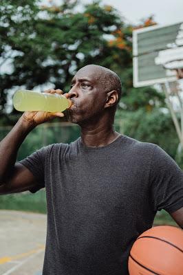 Black Man drinking a sports drink and holding a basketball after a workout