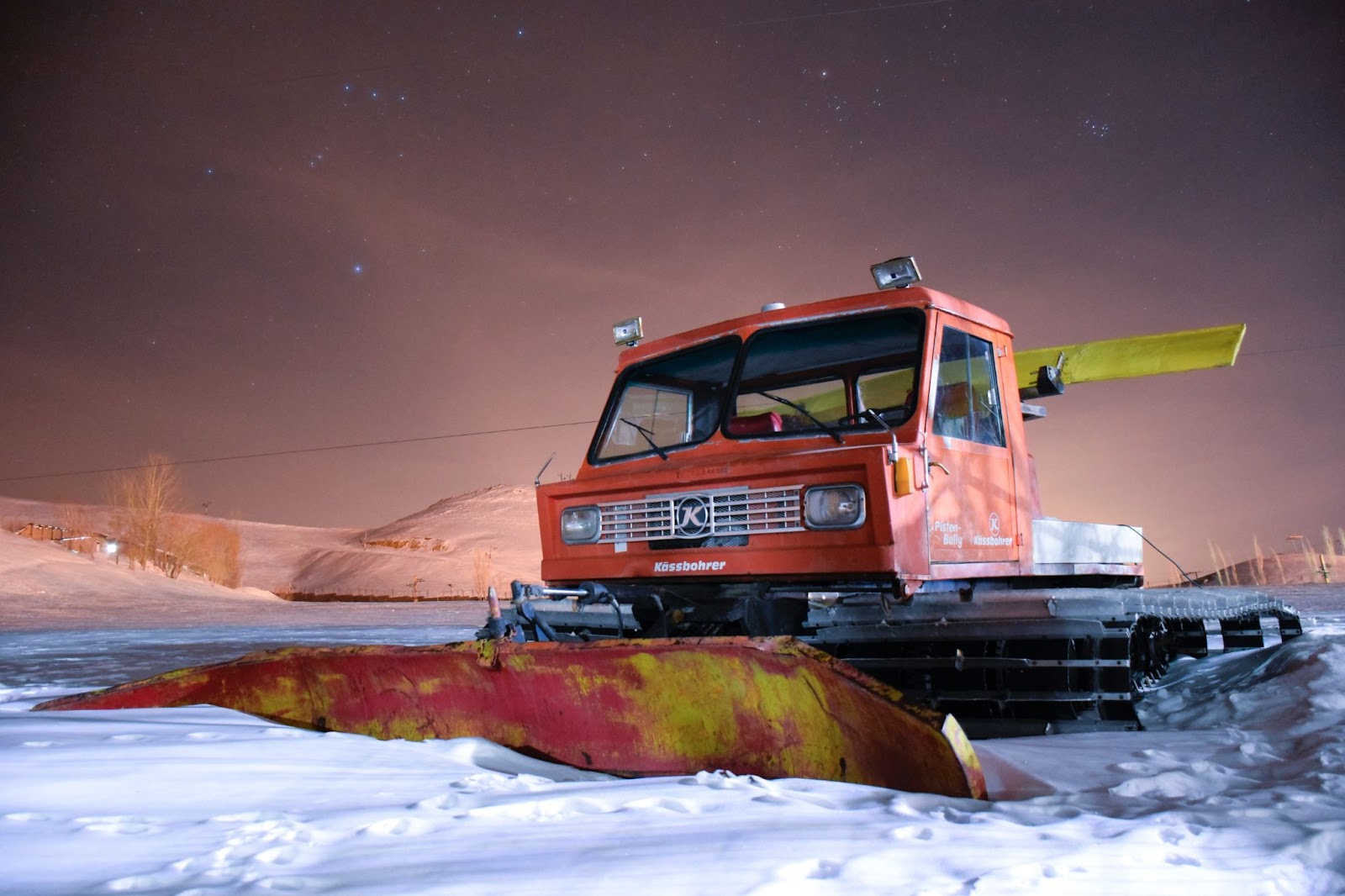 A snow plow in the middle of a snowy field at night