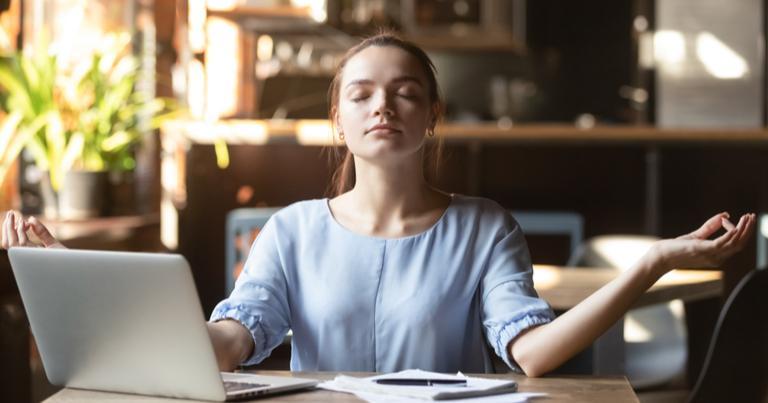 Una mujer de negocios meditando en una mesa de despacho con los ojos cerrados.