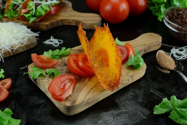 Keto taco cheese shell placed on top of tomato slices, served on a wooden board